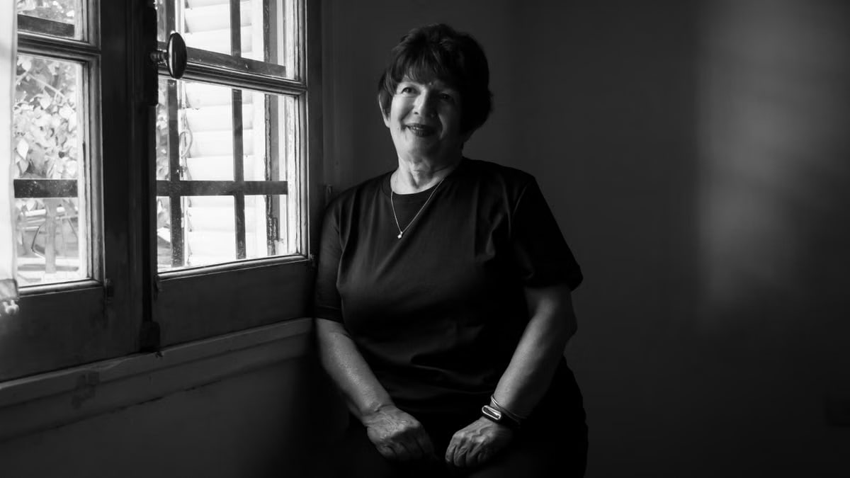 A senior woman smiling by the window, captured in black and white, evoking a warm and serene mood.